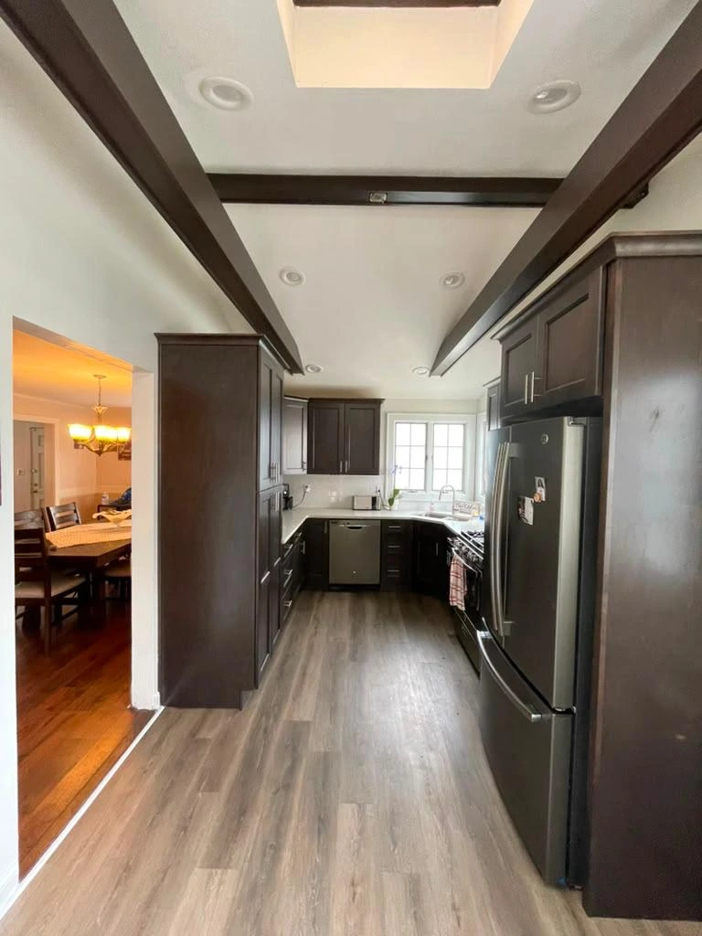 Modern kitchen with dark wood cabinets, stainless steel appliances, and wood-look flooring.