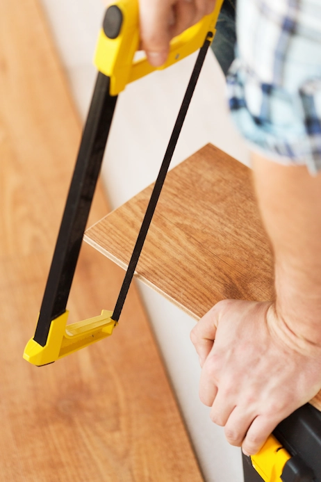 Engineered hardwood flooring installation with a worker cutting a wood plank for stairs.